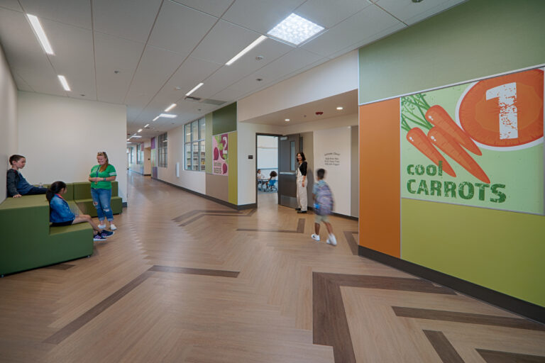 Bright school hallway with children, a teacher, and a large “Cool Carrots” poster on the wall