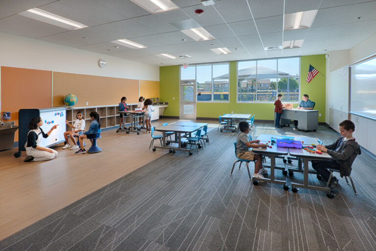Bright elementary classroom with children doing group activities and a teacher at the front