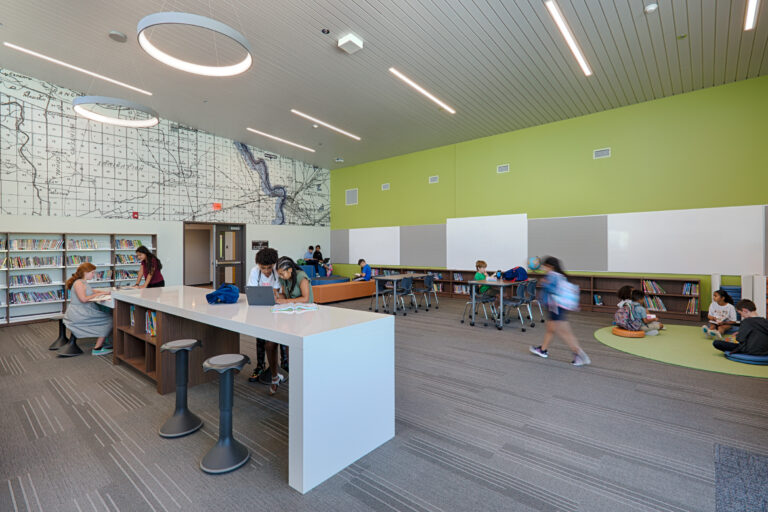 Modern school library with students reading at tables, bookshelves, and a large map mural on the wall