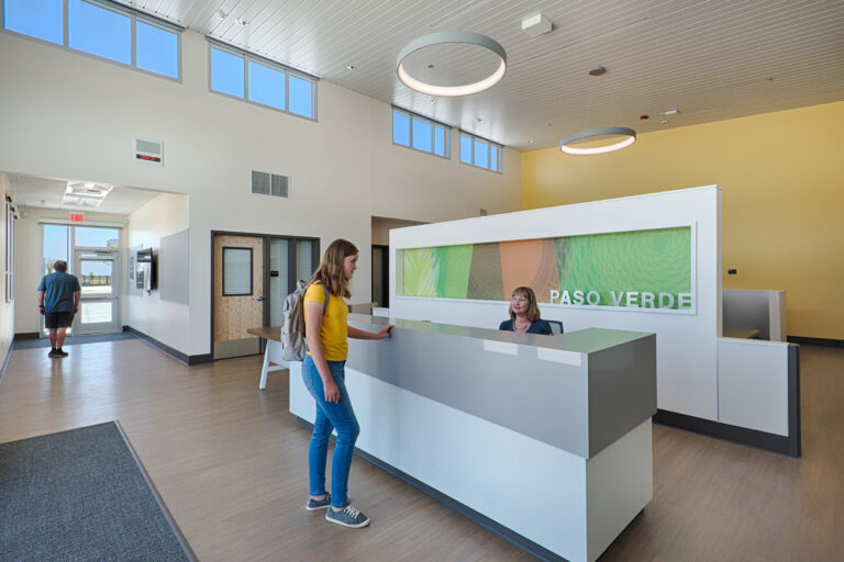 Modern lobby reception area with a woman speaking to a receptionist and PASO VERDE signage behind them