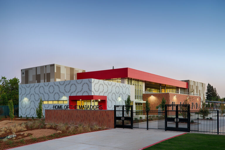 Modern school building with red and patterned gray facades, sign reading Home of the Matadors, at dusk