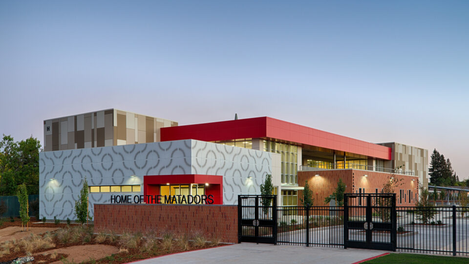 Modern school building with red and patterned gray facades, sign reading Home of the Matadors, at dusk