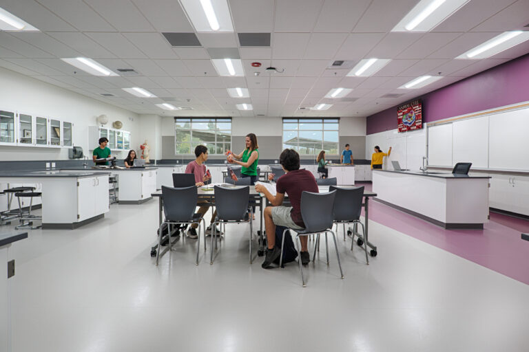 Students and a teacher collaborate in a bright science classroom with lab tables and whiteboards