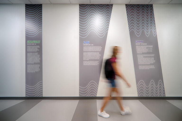 Blurred woman walking past wall panels labeled ultraviolet, X-ray, and gamma in a hallway