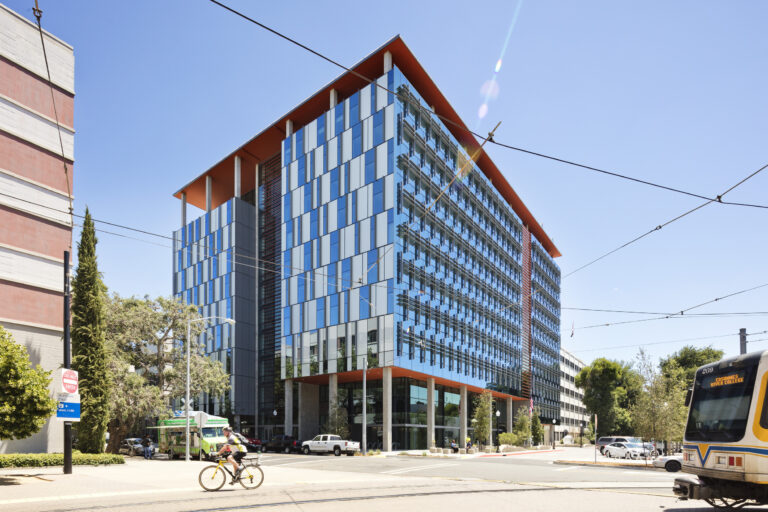 Modern glass office building on a sunny city street with a cyclist and a passing light-rail train
