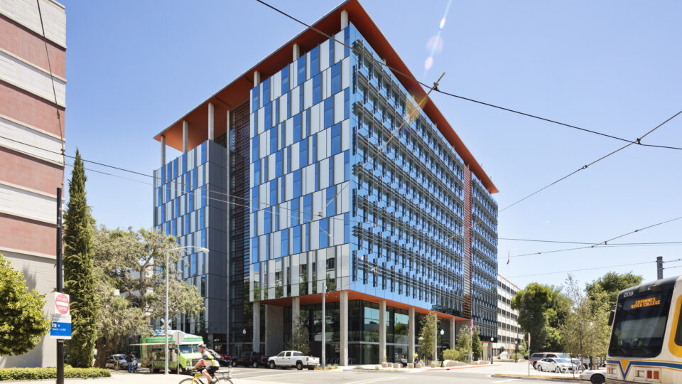 Modern glass office building on a sunny city street with a cyclist and a passing light-rail train