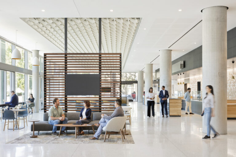 Modern office lobby with people seated and standing among tall columns, lounge seating, and large windows
