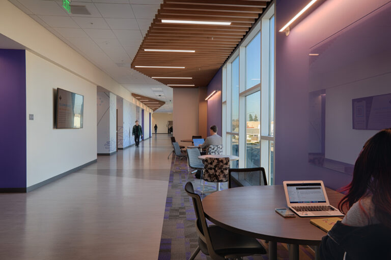Modern office hallway with seating areas, large windows, and people working on laptops
