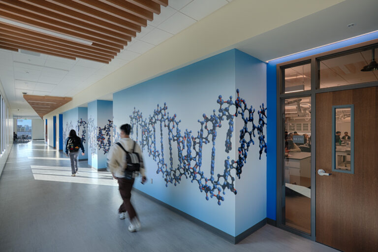 Modern hallway with a DNA mural, glass classrooms, and two students walking by