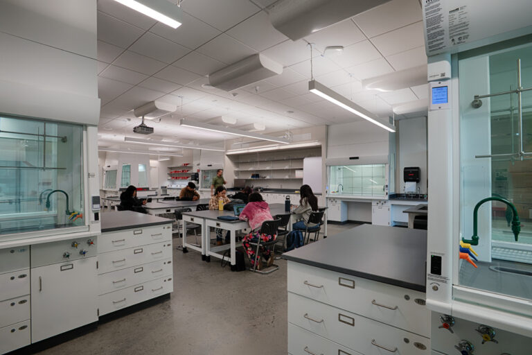 Modern chemistry lab with students seated at benches working on laptops and experiments