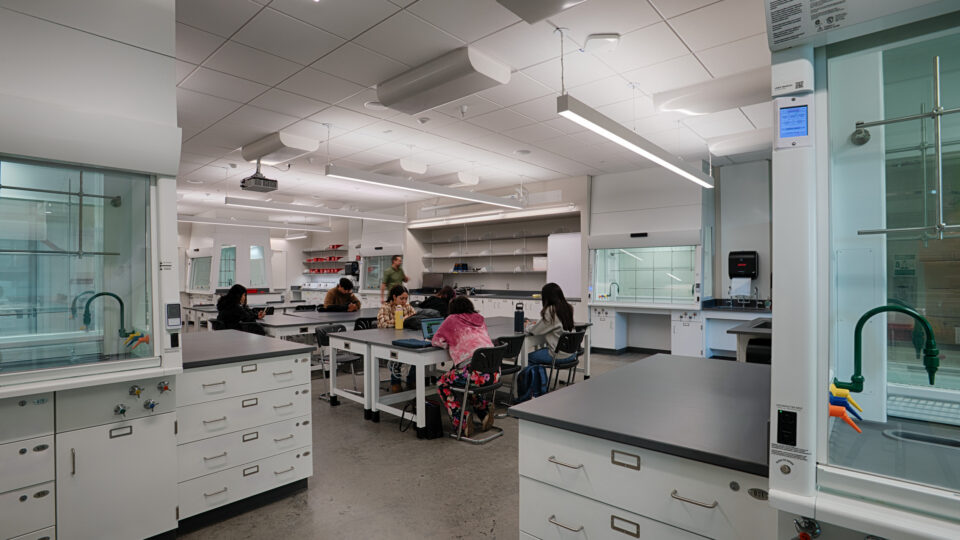 Modern chemistry lab with students seated at benches working on laptops and experiments