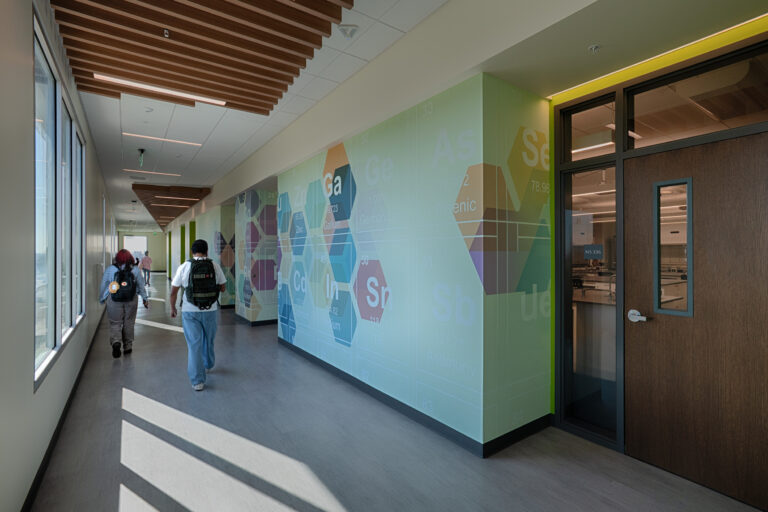 Students walking down a modern hallway with periodic table wall art and classroom doors