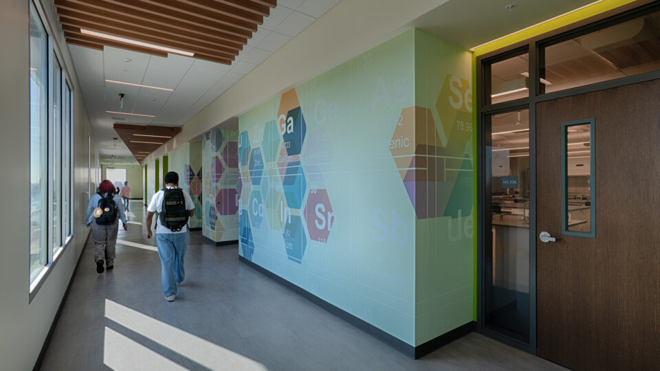 Students walking down a modern hallway with periodic table wall art and classroom doors