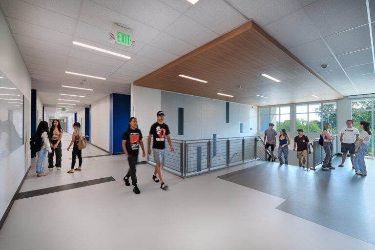 Students walking and talking in a modern school hallway with large windows and an exit sign overhead