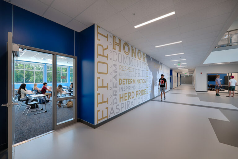 Modern school hallway with a classroom visible through glass doors and students walking past a wall of values words