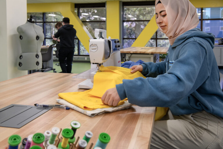 Woman in a hijab sewing yellow fabric on a machine in a bright workshop