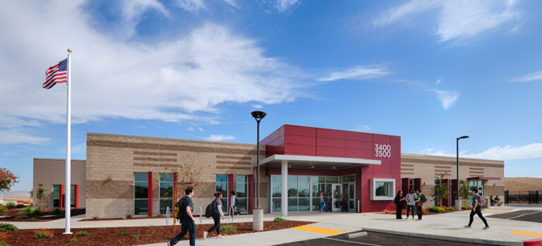Modern school building with students outside, an American flag, and a bright blue sky with wispy clouds