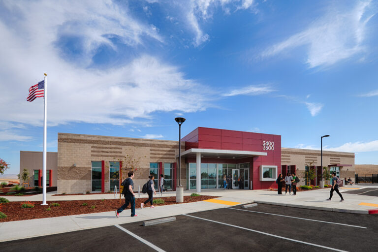 Modern school building with students outside, an American flag, and a bright blue sky with wispy clouds