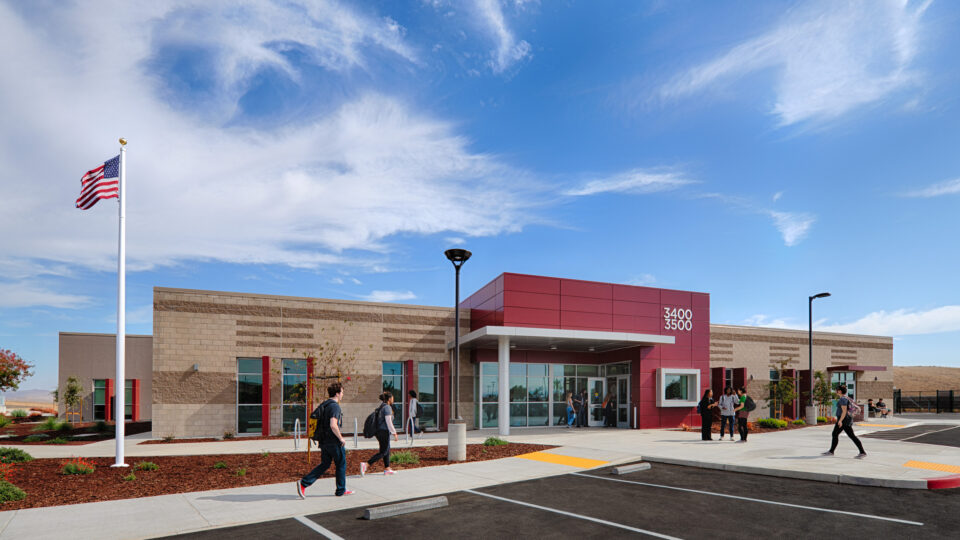 Modern school building with students outside, an American flag, and a bright blue sky with wispy clouds