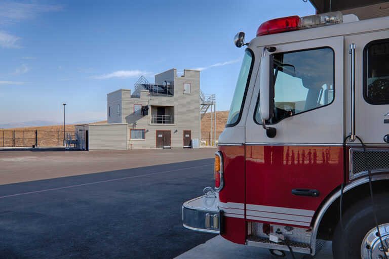 Fire truck parked beside a training tower under a clear blue sky