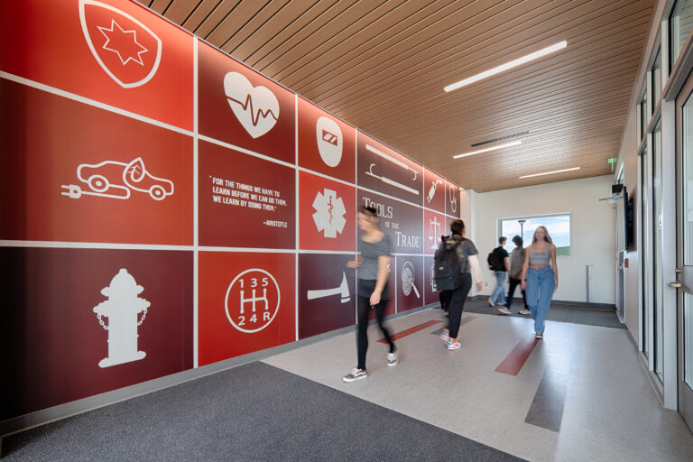 Students walking through a modern hallway with a red medical-themed mural and icons on the wall