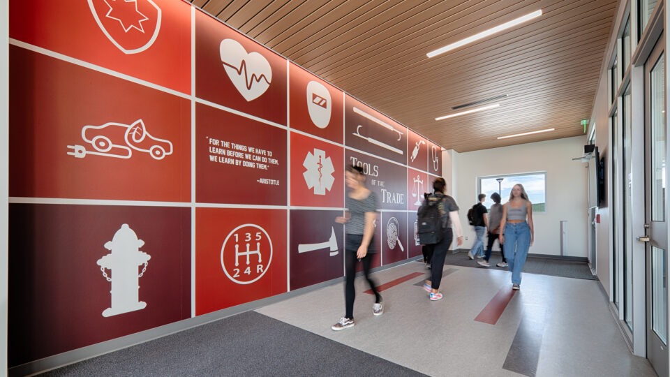 Students walking through a modern hallway with a red medical-themed mural and icons on the wall