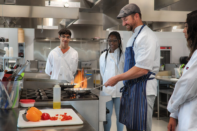 Chef teaching students in a commercial kitchen while cooking at a flaming stove