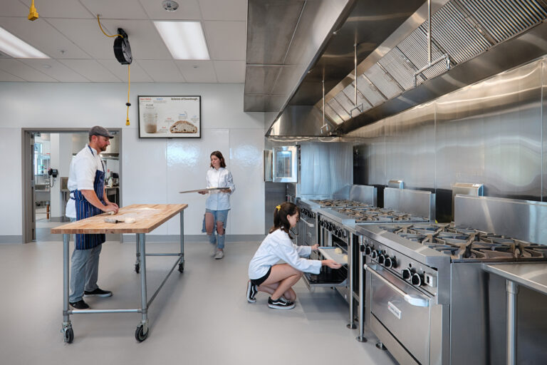 Chefs working in a modern stainless-steel commercial kitchen with a large stove and prep table