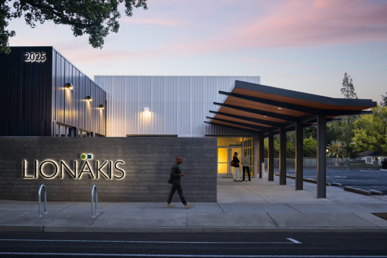 Modern building entrance at dusk with illuminated LIONÁKIS and 2025 signs and a covered walkway