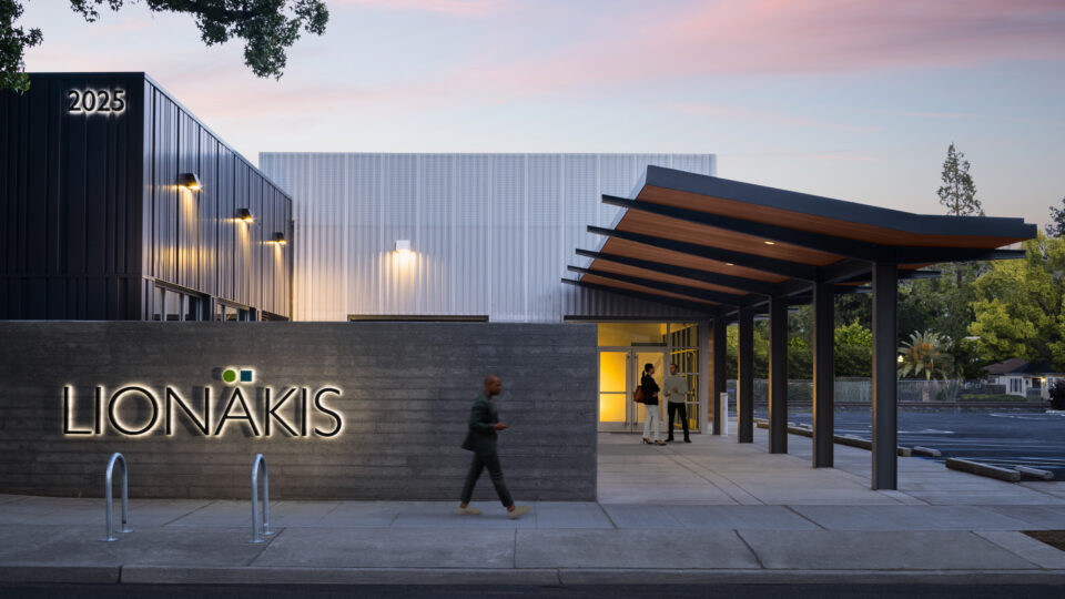 Modern building entrance at dusk with illuminated LIONÁKIS and 2025 signs and a covered walkway