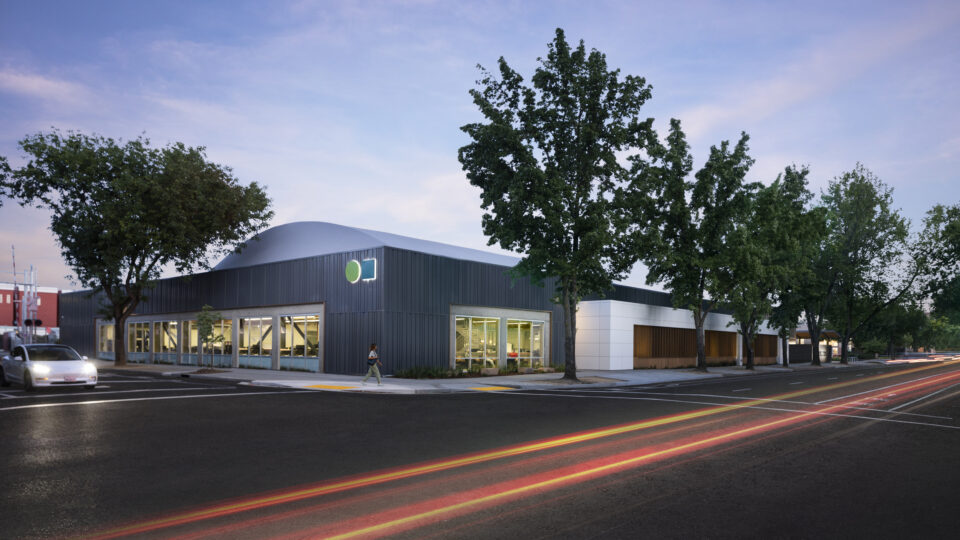 Modern corner building at dusk with large windows, trees, and light trails on a wet street