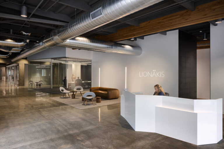 Modern office lobby with exposed ducts, glass meeting rooms, a white reception desk, and lounge seating on a rug