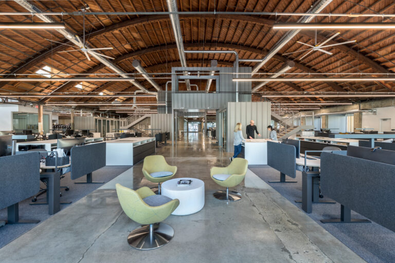 Open office interior with exposed wooden arched ceiling, workstations, and three lounge chairs in the center