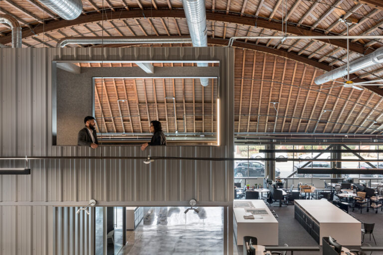 Two people talking on an interior balcony of a modern open office with exposed wood beams and ductwork