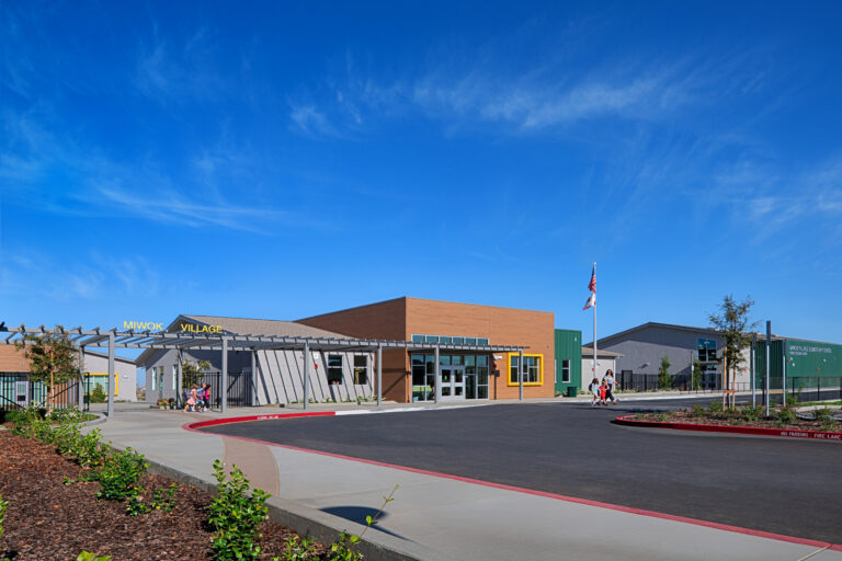 Modern elementary school campus entrance with children walking under a blue sky, labeled Miwok Village Elementary School