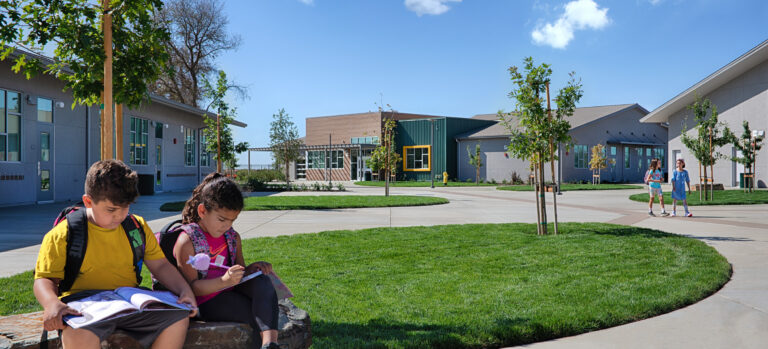 Children with backpacks sit and study on a stone bench in a sunny school courtyard
