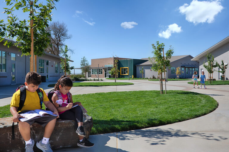 Children with backpacks sit and study on a stone bench in a sunny school courtyard