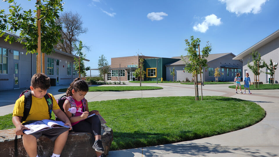 Children with backpacks sit and study on a stone bench in a sunny school courtyard
