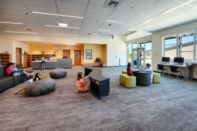 Bright modern library with children reading, sitting on beanbags, and using computers near a circulation desk