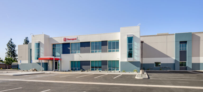 Modern Theragent office building with a mostly empty parking lot under a clear blue sky