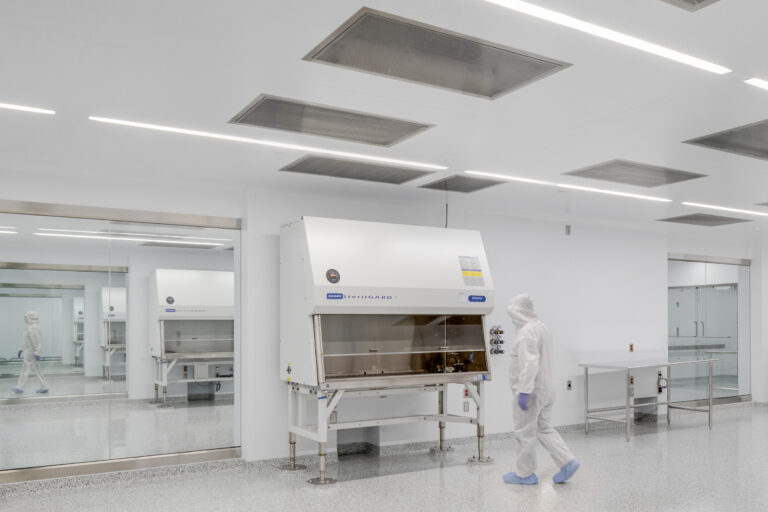 Cleanroom laboratory with a person in protective suit walking past a biosafety cabinet and glass partitions
