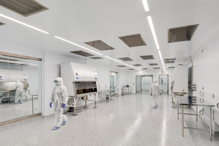 Cleanroom lab with two technicians in protective suits working beside large sterile cabinets and glass walls