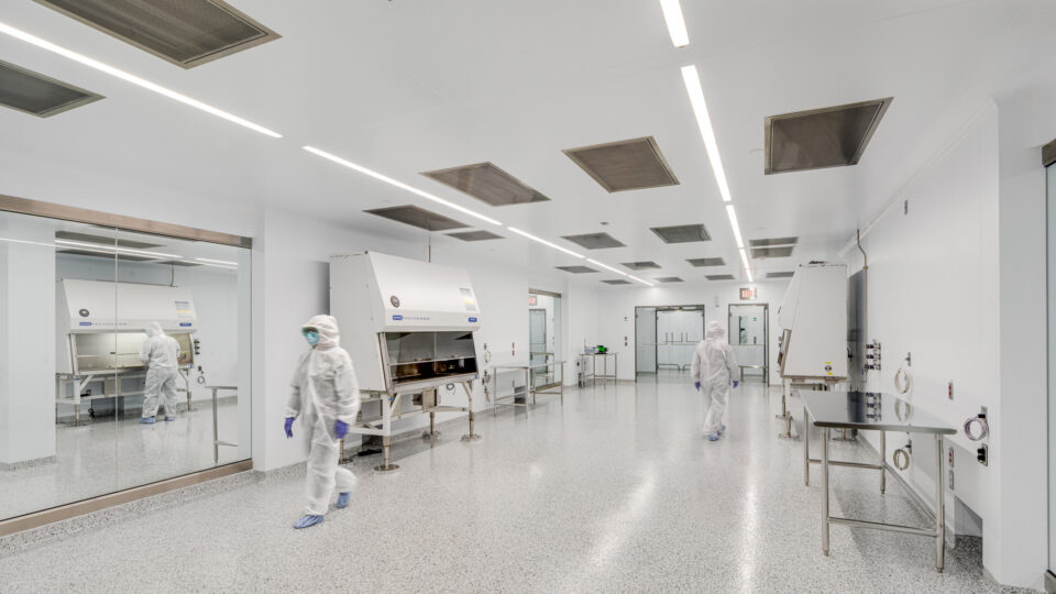 Cleanroom lab with two technicians in protective suits working beside large sterile cabinets and glass walls