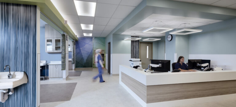 Modern hospital reception area with a nurse at the desk and another staff member walking past a sink