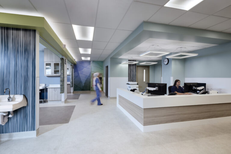 Modern hospital reception area with a nurse at the desk and another staff member walking past a sink