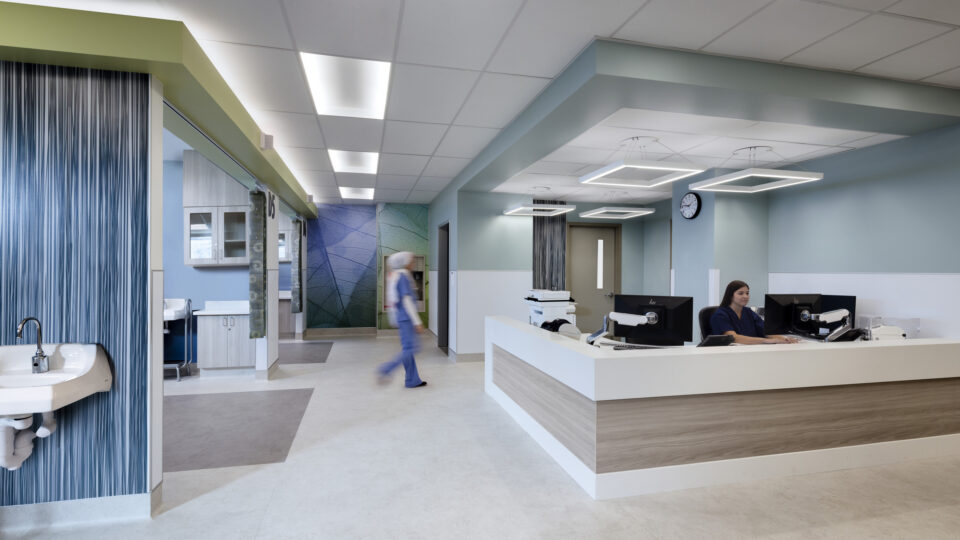 Modern hospital reception area with a nurse at the desk and another staff member walking past a sink