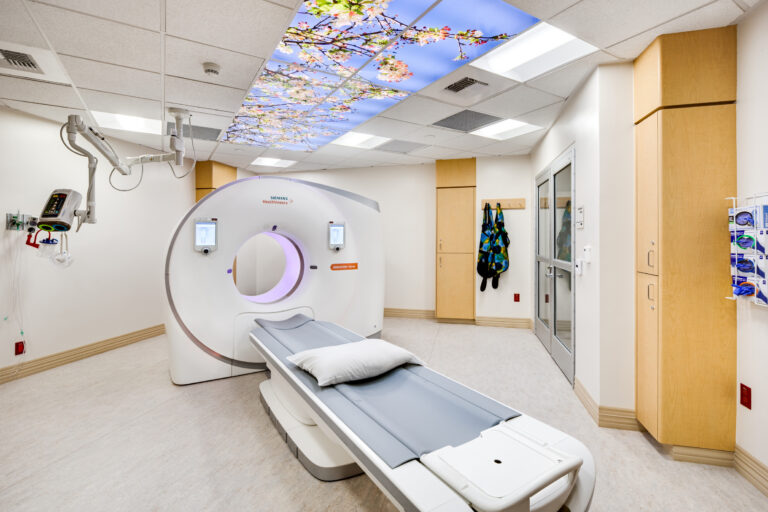 Hospital CT scan room with a patient table and a blossom-sky ceiling mural