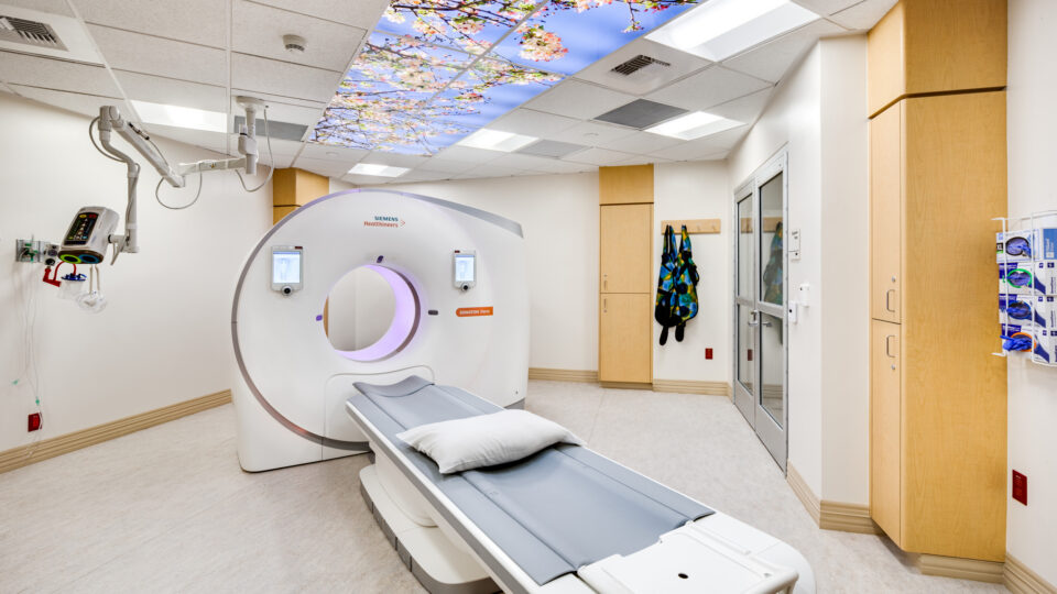 Hospital CT scan room with a patient table and a blossom-sky ceiling mural