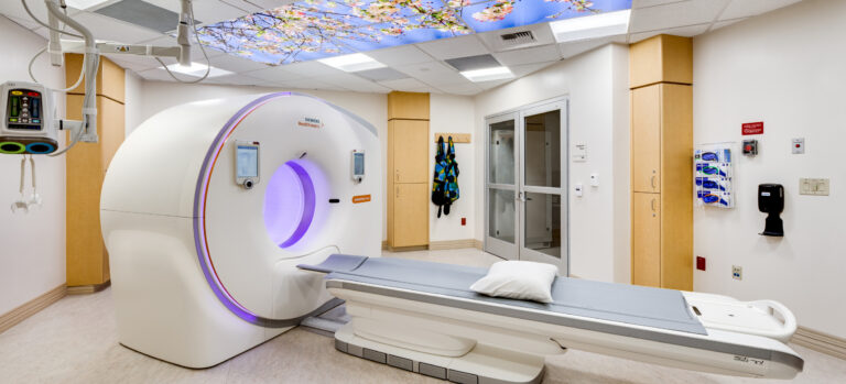 Hospital imaging room with a CT scanner, patient table, and a ceiling panel showing cherry blossoms