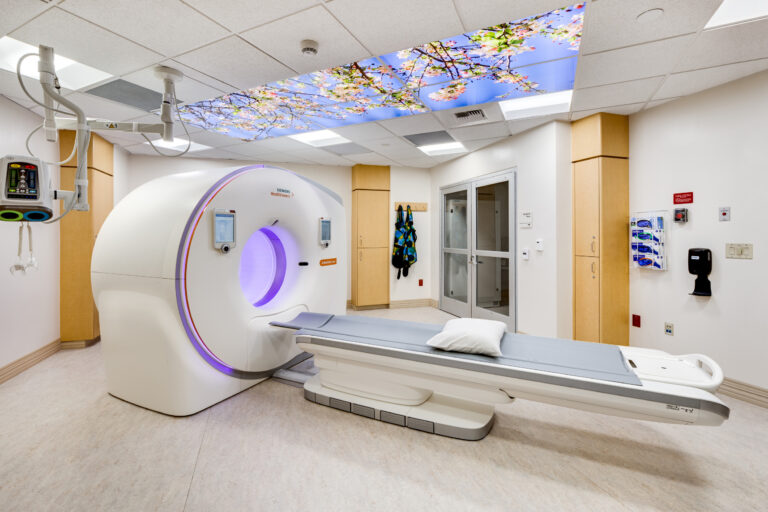 Hospital imaging room with a CT scanner, patient table, and a ceiling panel showing cherry blossoms
